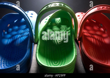 A row of  brightly coloured blue green and red Crocs clogs with light shining through the pattern of holes in the uppers Stock Photo