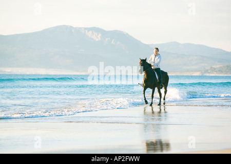woman riding a black horse on the beach Stock Photo