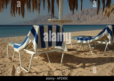 Two beach sun loungers with striped towels prepared for a day of sunbathing on the beach Stock Photo