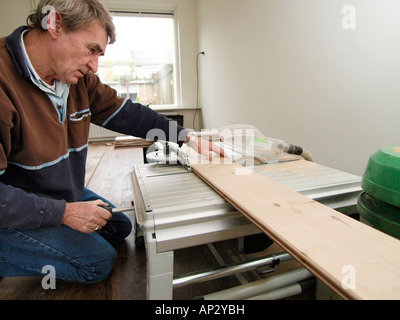 older gentleman using circular saw table when laying new parquet floor in living room Stock Photo