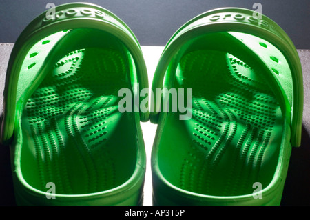 A pair of bright green Crocs clogs with light shining through the pattern of holes in the uppers Stock Photo