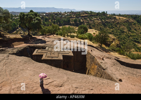 A lone local woman with a pink umbrella looks over the Bete Giyorgis or Church of St. George monolithic church in Lalibela. Stock Photo