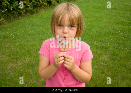 Young girl blowing a dandelion against a green grass background Stock Photo