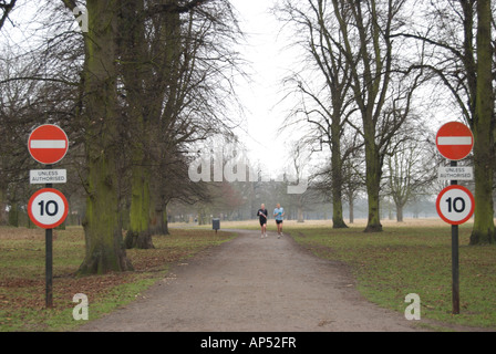 Mounted on poles, british road signs stand on either side of a lane in bushy park, england, as two female joggers approach Stock Photo