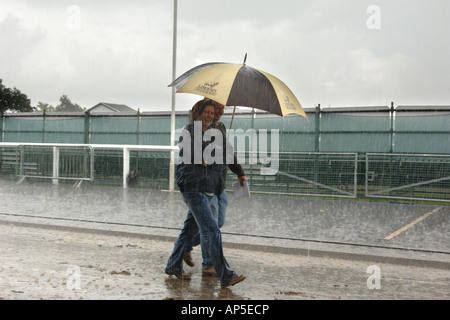 Two people walking in a rain storm along a road in England Stock Photo