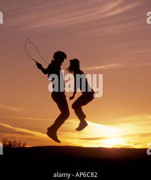 young man and woman jumping rope on hill at sunset Stock Photo