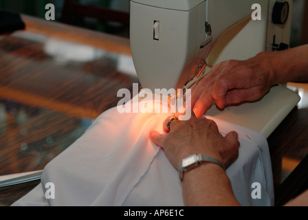 Close up of a woman using a domestic sewing machine to sew white cotton material. Stock Photo