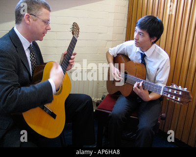 A student during a guitar tutorial by his teacher Stock Photo