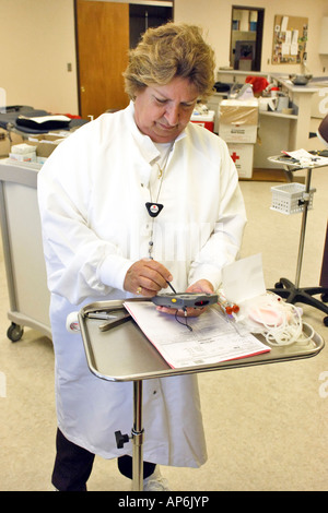 Nurse checking a patients data into a PDA machine prior to taking blood Stock Photo