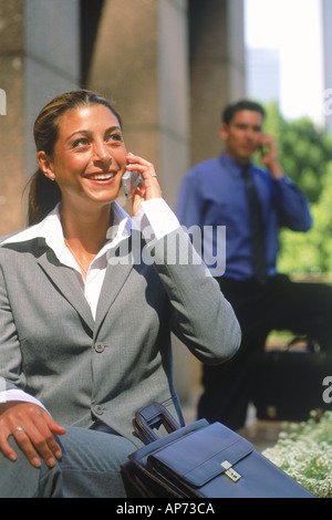 Hispanic businesswoman talking on cellphone with man behind in downtown Los Angeles Stock Photo