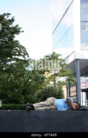 Man asleep on a wall in the redeveloped Spitalfields area of East London Stock Photo