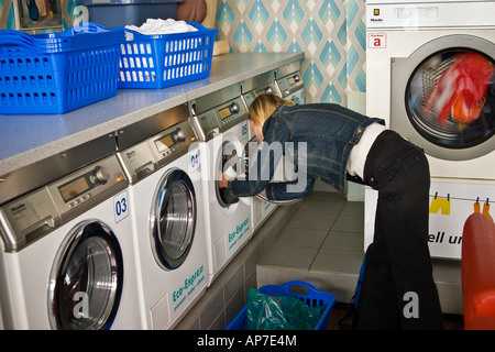Doing laundry at a German eco friendly laundromat Young woman putting clothes into a washing machine Stock Photo
