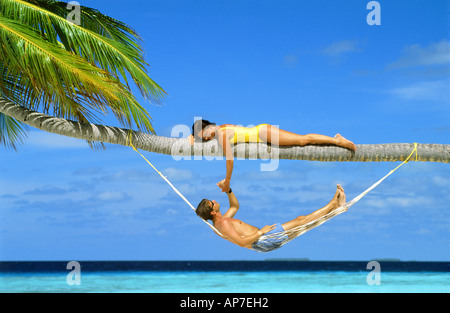 Couple holding hands on palm tree above sandy beach on Fihalhohi Island in South Male Atoll of Maldive Islands Stock Photo