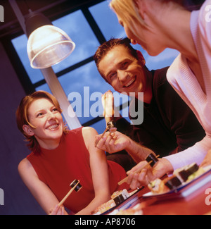 Two businesswomen and businessman eating sushi in bar Stock Photo