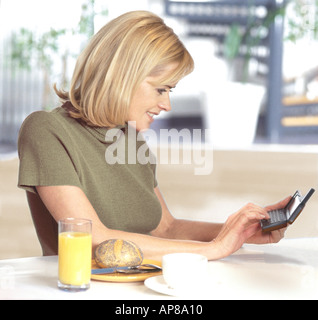 Side profile of a young woman using a PDA at a breakfast table Stock Photo