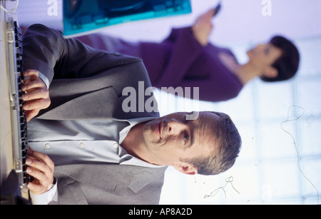 Businessman working on a computer with a businesswoman standing in the background Stock Photo