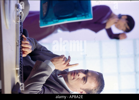 Businessman working on a computer with a businesswoman standing in the background Stock Photo