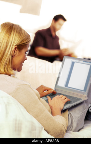 Rear view of woman using laptop on sofa with man in background Stock Photo