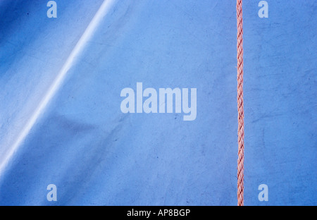 Detail of white plastic or nylon tarpaulin sheet with a highlighted fold in it and bisected by pale orange nylon rope Stock Photo