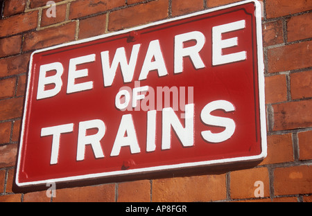 Bold cast iron metal sign painted white on scarlet red and fixed on orange brick wall stating Beware of trains Stock Photo