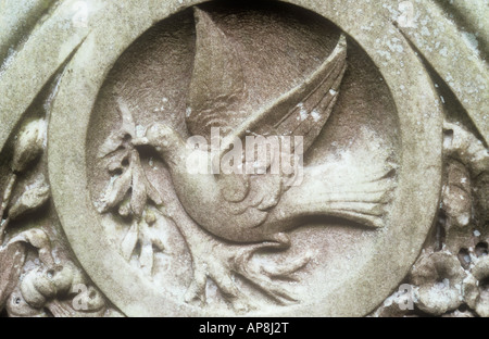 Detail of stone gravestone into which has been carved a dove with wings open sitting on branch and carrying sprig of olive Stock Photo