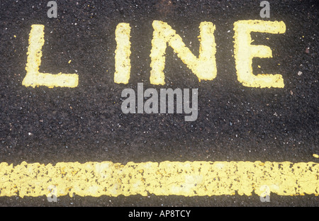 Pale yellow line painted on black tarmac and above it the painted word LINE Stock Photo