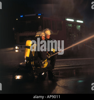 Two firemen spraying water on fire with hose Stock Photo