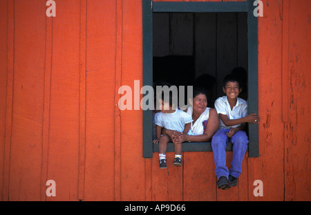 Locals in the window of their orange painted home shop awaiting the saints procession San Sebastian Retalhuleu Guatemala Stock Photo