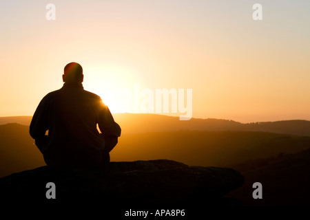 Silhouette profile of a man sat in meditation on a hill  at sunrise Stock Photo