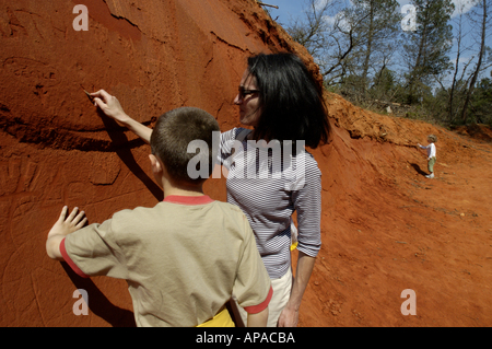 France Provence The Rustrel Canyon Young Boy And His Mother Drawing Their Names On A Red Sandy Cliff Stock Photo