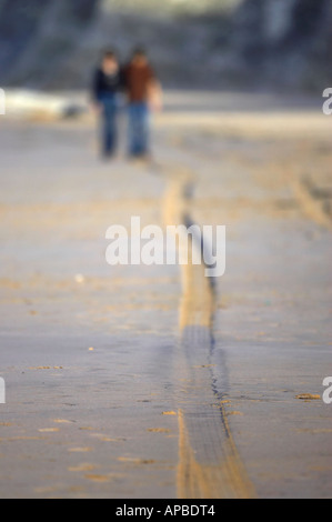 young couple walking along the beach with tyre tracks white rocks beach portrush county antrim northern ireland Stock Photo