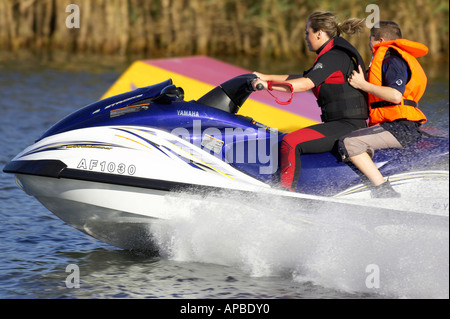 young woman in wetsuit driving a yamaha 4 stroke AF1030 waverider with young boy passenger at speed past a floating water ski ju Stock Photo