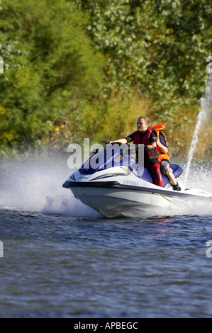 young woman in wetsuit driving a yamaha 4 stroke AF1030 waverider with young boy passenger at speed Stock Photo