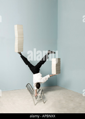 business man balances stacks of papers while doing a handstand on a chair in the office balance multi task Stock Photo