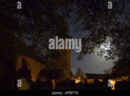 Full moon shining through leaves of trees above graveyard stones in St Brannock’s Parish Church Braunton Devon England Stock Photo