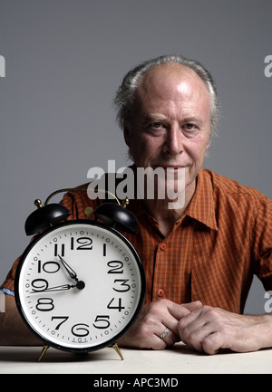 Mature man sitting at a table with an alarmclock Stock Photo