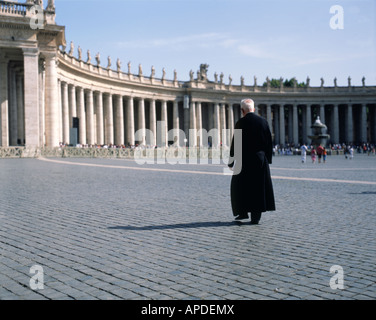 Black dressed single priest walking across St. Peter's Square with the columns of colonnade in the background, Vatican, Rome Stock Photo