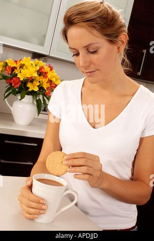 WOMAN IN KITCHEN DUNKING BISCUIT INTO CUP OF TEA Stock Photo