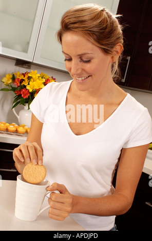 WOMAN IN KITCHEN DUNKING BISCUIT INTO CUP OF TEA Stock Photo