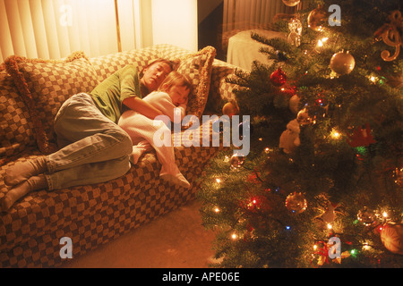 Mother and daughter sleeping on sofa next to Christmas tree Stock Photo