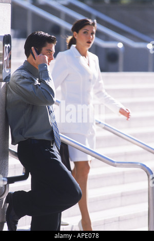 Businessman talking on cellphone with businesswoman passing Stock Photo