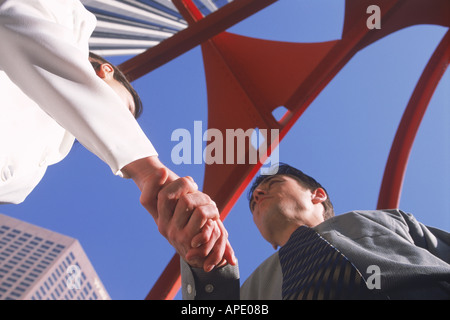 Businessman and woman shaking hands under Four Arches sculpture designed in1974 by Alexander Calder in downtown Los Angeles Stock Photo