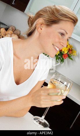 WOMAN IN KITCHEN DRINKING GLASS OF WHITE WINE Stock Photo