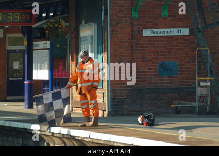 Shenfield railway station platform with lookout holding out chequered black and white flag to signal track workers ahead Stock Photo