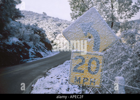 Winter snow on slow curve turn speed warning arrow sign along rural country two lane mountain road Alameda County California Stock Photo