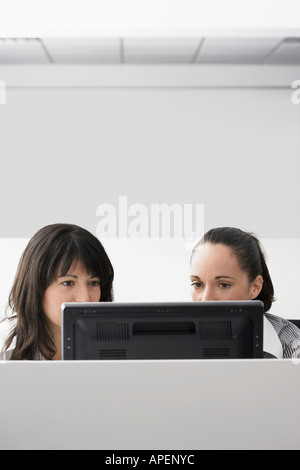 Two female office workers using computer in office cubicle Stock Photo