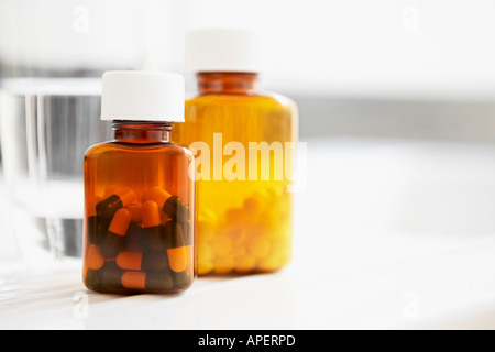 Two bottles of pills and glass of water on table, close up Stock Photo