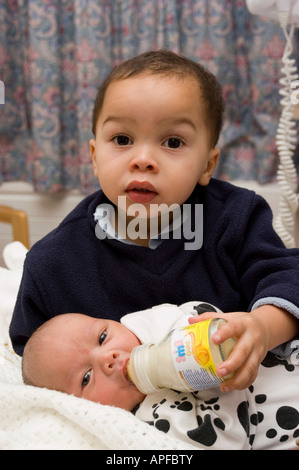 Two year old boy feeds new born baby bottled milk Stock Photo