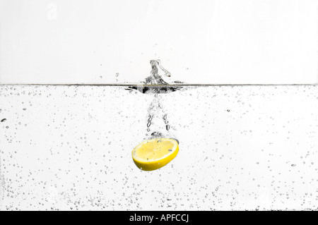 Slice of lemon splashing dropping into fizzy carbonated water Stock Photo