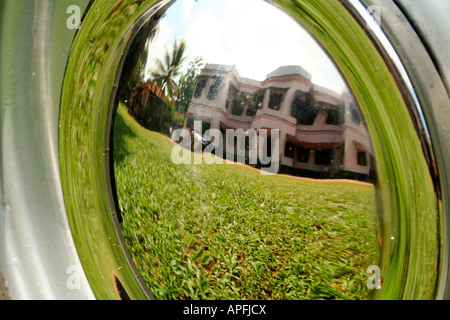 Typical big old house with well maintained lawn in Kerala, reflected on the silver plated wheel-cup of an ambassador car Stock Photo